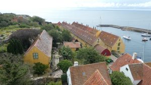 Luftfoto af Christiansø med de gule længehuse, havnen og Østersøen omkring øen